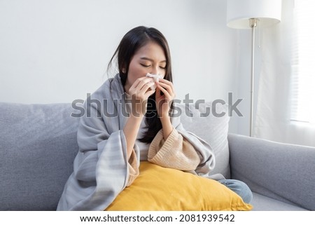 Young Sick Asian Woman Sitting under the Blanket Whiles Sneezing  with Tissue on the Sofa