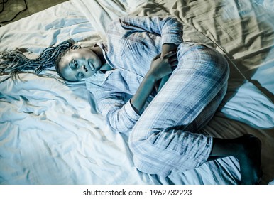 Young Sick And Depressed Afro American Woman In Pajamas Lying On Bed Suffering Menses And Period Pain Feeling Unwell Holding Her Stomach Sleepless At Night