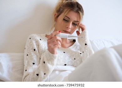 Young Sick Girl With Fever Checking Her Temperature With A Thermometer At Home