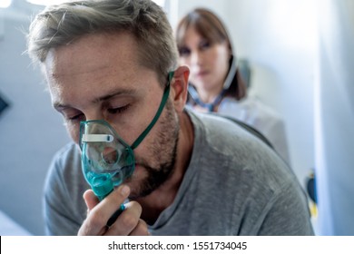 Young Sick Man Patient With Oxygen Mask While Female Doctor Listens His Chest With Stethoscope In Hospital Emergency Room. In Smoking And Respiratory Diseases And Anti Tobacco Advertising Campaign.