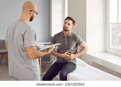 Young sick man sitting on the couch in the doctor's office and pointing to stomach during medical examination in clinic. Physician male doctor listening to the patient's complaints. - Powered by Shutterstock