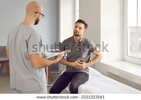 Young sick man sitting on the couch in the doctor's office and pointing to stomach during medical examination in clinic. Physician male doctor listening to the patient's complaints.