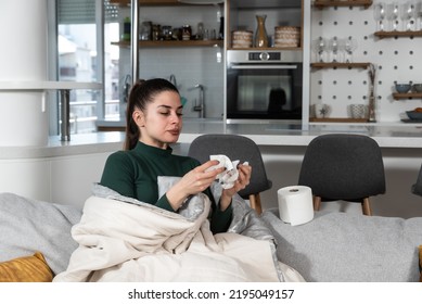 Young sick stressed woman lying at home covered with blanket blowing her nose. Ill female have common cold and flue with runny nose allergy reaction wipe it with paper tissue. - Shutterstock ID 2195049157