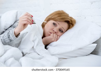 Young Sick Woman In Bed Checking Body Temperature With Thermometer Looking Bad , Feverish And Weak Suffering Winter Cold Virus Like Flu And Influenza In Illness And Disease Vs Health Care Concept 