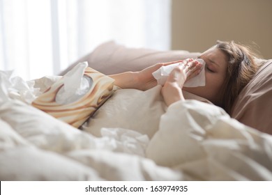 Young Sick Woman Blowing Her Nose While In Bed