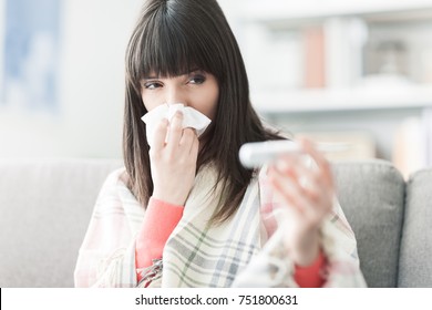 Young Sick Woman With Cold And Flu, She Is Blowing Her Nose And Measuring Her Body Temperature