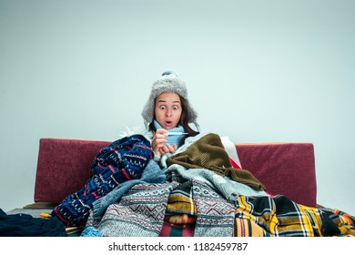 The Young Sick Woman With Flue Sitting On Sofa At Home Or Studio Covered With Knitted Warm Clothes. Illness, Influenza, Pain Concept. Relaxation At Home. Healthcare Concepts.