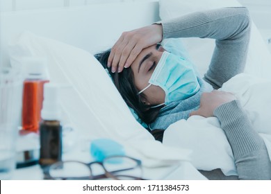 Young Sick Woman Lies Tired In Bed With A Face Mask And Holds Her Head Because Of A Headache.