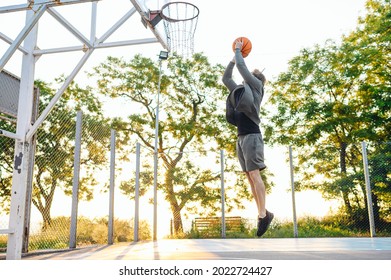 Young side view sporty strong caucasian sportsman man wearing sports clothes training shooting free throw jump playing with ball at basketball game playground court. Outdoor courtyard sport concept.