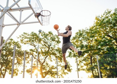 Young Side View Sporty Strong Sportsman Man Wearing Sports Clothes Training Shooting Free Throw Flying High Jump Playing With Ball At Basketball Game Playground Court Outdoor Courtyard Sport Concept.