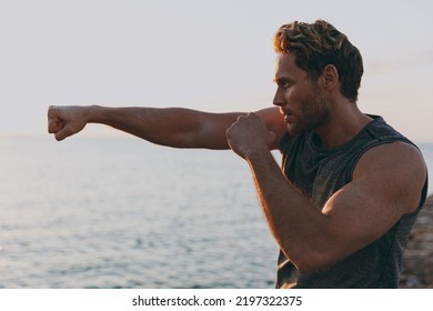 Young side view sporty strong athletic toned fit sportsman man in sports clothes warm up train boxing clenching fist at sunrise sun dawn over sea beach outdoor on pier seaside in summer day morning. - Powered by Shutterstock