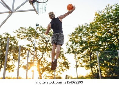 Young Side View Strong Sportsman Man In Sports Clothes Training Shooting Free Throw Fly High Jump Scoring Basket Playing With Ball At Basketball Game Playground Court Outdoor Courtyard Sport Concept.