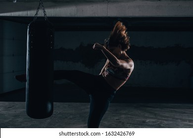 Young silhouette female practicing high kick with the boxing bag inside the garage. - Powered by Shutterstock