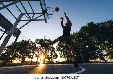 Young Silhouette Strong Sportsman Man In Sports Clothes Training Shooting Free Throw Fly High Jump Scoring Basket Play With Ball At Basketball Game Playground Court Outdoor Courtyard Sport Concept.