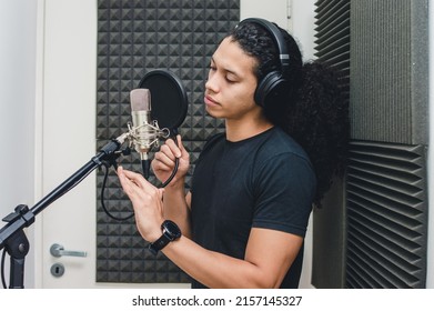 Young Singer Man With Headphones Inside The Professional Studio In The Recording Booth, Fixing The Anti Pop Filter And The Microphone To Sing And Record A Song.