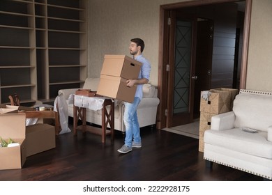 Young Single Man Carrying Big Packed Cardboard Boxes With Personal Belongings Inside Unfurnished Living Room On Relocation To New First Own Or Rented House. Homeowner Move Day, Tenancy, Bank Mortgage