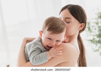 Young single mother lulling cradling her crying little small son daughter toddler infant newborn baby. Colics, teething health problems. Postnatal depression. Motherhood and childcare