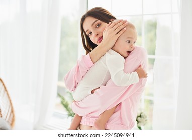 Young single mother lulling cradling her crying little small son daughter toddler infant newborn baby. Colics, teething health problems. Postnatal depression. Motherhood and childcare.