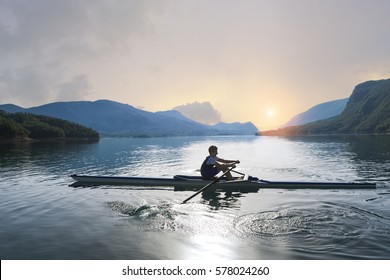 A Young single scull rowing competitor paddles on the tranquil lake - Powered by Shutterstock