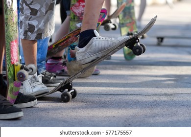 Young Skate Boarders At Street Summer Competition.Skaters With Skateboards Compete In Skatepark Outdoor.Big Crowd Of Young Athletes Ready To Roll.Dirty Cheap Sneakers On Poor Boy Feet