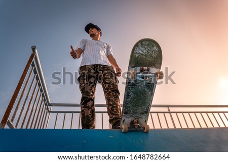 Young skateboarder on top of the ramp steps on the skate at sunset. View from below