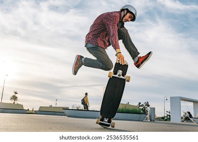 Young skateboarder skillfully jumps on his longboard at a vibrant skate park during sunset, capturing the energy and movement of this action-packed sport - Powered by Shutterstock