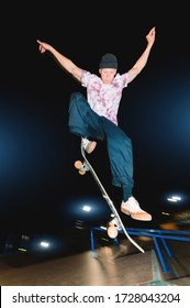 A Young Skatecrack In A Night Skatepark Does A Halfpipe Jump Jump. Youth Culture Leisure Concept At Night