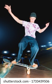 A Young Skatecrack In A Night Skatepark Does A Halfpipe Jump Jump. Youth Culture Leisure Concept At Night