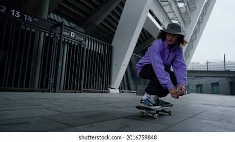 Young skater boy making kickflip trick in city stadium in slow motion. Sporty hipster jumping on skate outdoor in summer. Active male person practicing extreme sports in downtown.