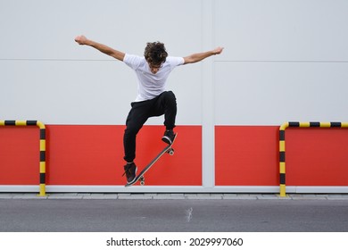 young skater does tricks outdoor. background is white and red wall