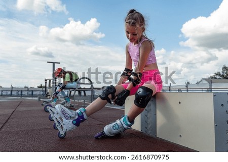 Young skater girl putting on protective shin guards and knee pads for skating. children female rollerblader preparing for a ride in skatepark in summer