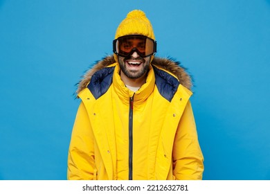 Young Skier Man 20s Wearing Yellow Puffer Down Jacket With Fur Hood Googles Mask Look Camera Isolated On Plain Blue Color Background Studio Portrait. People Winter Lifestyle Sport Activity Concept.