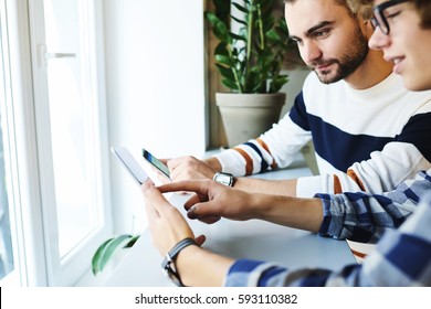 Young skilled male IT developers testing usability of application for modern digital devices sharing multimedia files via online chat using smartphone and portable pc connected to 5G wireless