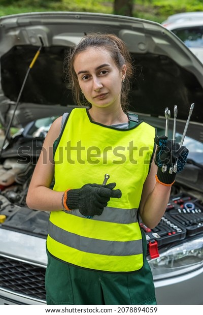 young skilled specialist mechanic\
woman in overalls and tools in hands near broken car. Mechanic\
woman concept. The concept of a car with a breakdown on the\
road