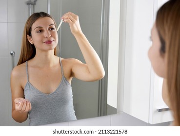 Young Skin Care Routine. Beautiful girl applying a Vitamin C booster antioxidant ascorbic acid anti aging serum to her face while holding a pipette in her hand.