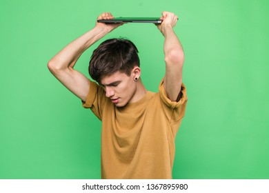 Young Skinny Guy Throwing Laptop On Floor Standing On Green Background In Studio