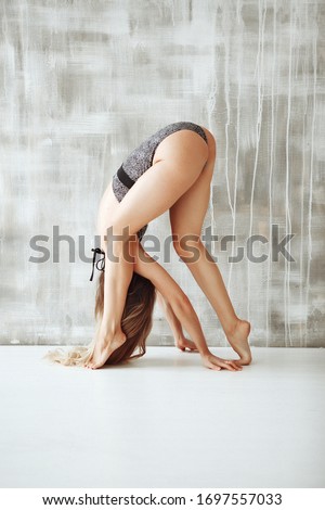 Young skinny woman in grey leotard doing yoga in light grey studio in her home during quarantine. What to do at home during self-isolation. Stay home