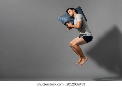 Young Sleeping Man Holding His Pillow Levitating In Empty Gray Room Background With Copy Space