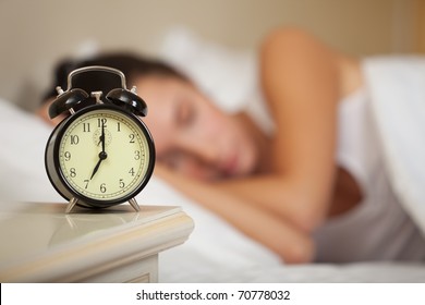 Young Sleeping Woman And Alarm Clock In Bedroom At Home.