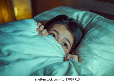 young sleepless beautiful and scared Asian Chinese woman lying on bed awake at night suffering nightmare after watching zombie horror movie in fear and stressed face expression 