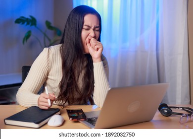 Young sleepy Asian woman sitting in front of computer yawning over worked at night, Asian female student  study online at night. 