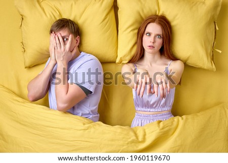 Young sleepy man lying on bed with wife suffering from somnambulism
