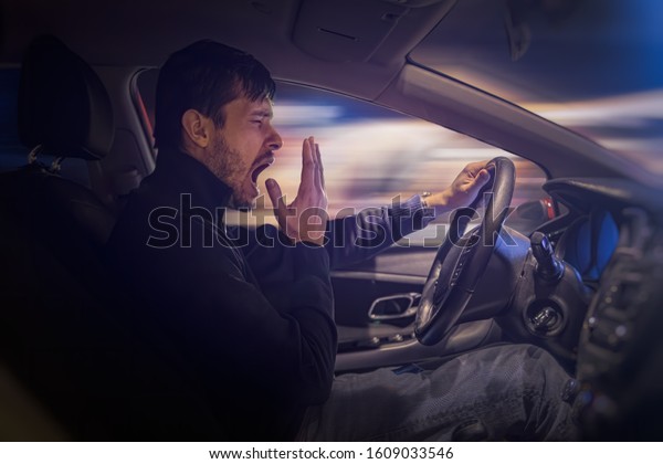 Young\
sleepy man is yawning and driving car at\
night.