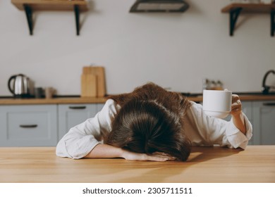 Young sleepy tired sad european housewife woman wearing casual clothes put head on table drinking coffee ask to pour eating breakfast cooking food in light kitchen at home alone. Healthy diet concept - Powered by Shutterstock