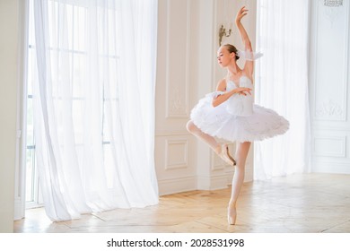 young slender ballerina in a white tutu in pointe shoes is dancing in a large beautiful white hall.