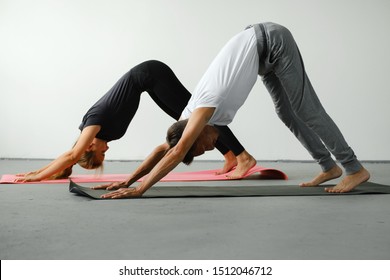 A Young Slender Girl And A Young Man Do Yoga. They Stand On A Yoga Mat In A Dog Pose Face Down.