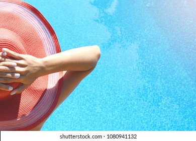 A young slender girl in a swimsuit and hat sits by the pool and takes sunny procedures (sunbathing). Summer time 
