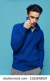 a young and slender man with thick black hair standing on a blue background in a blue zip-up sweater with a white T-shirt under it.Vertical studio shot.