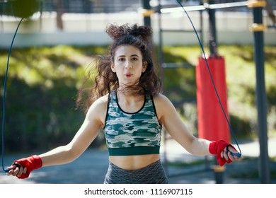 Young slender woman jumping with a rope, boxing workout outdoors at sunny day - Powered by Shutterstock