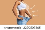 Young slim african american female in big jeans enjoy weight loss result with fat abstract body around, arrows isolated on beige wall background, studio. Diet, health and body care, before and after
